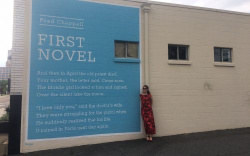 Walk leader Amy Bagwell, artist and poet, in front of one of the 20 Wall Poems painted around Charlotte. The poem by Greensboro poet Fred Chappell at East Ninth and North Brevard streets was on the May 17 Uptown Wall Poems walk. Photo: Mary Newsom