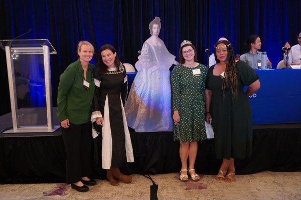 A group of women standing in from of a conference stage smiling.