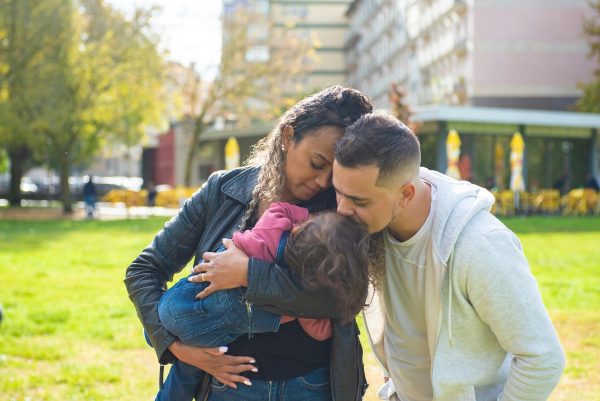 A man kissing his child while in the mother's arms.