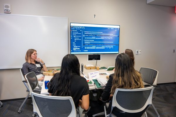 A group of women sitting at a table in front of a mounted TV.