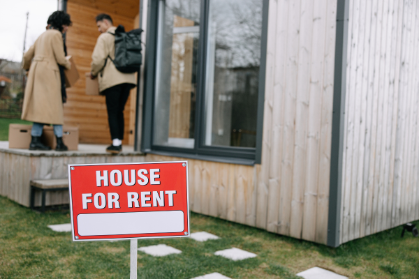 House with rent sign on front lawn and two people in the background.