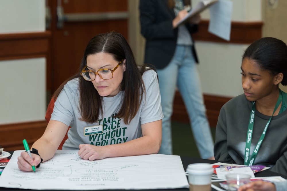 Liz Morrell, Ph.D., Director of Public Policy Research at the Charlotte Urban Institute, writes on a large sheet of paper during a group activity at the 2024 Women and Girls Research Alliance Leadership Cafe.