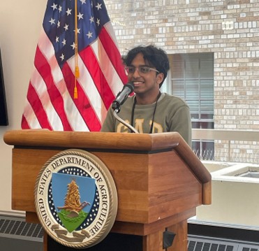 Vrishab Nooka standing at a podium in a government office.