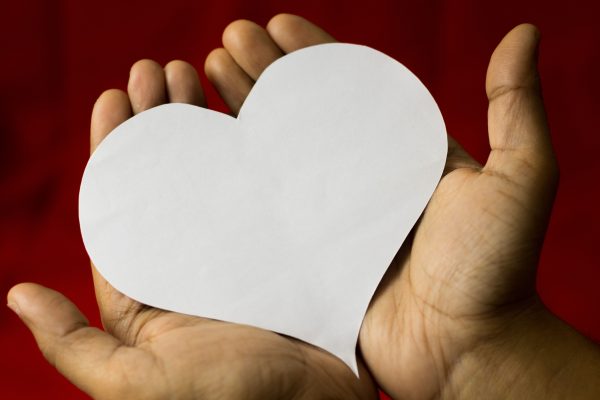 hands cradling a heart-shaped paper, symbolizing love on a red background